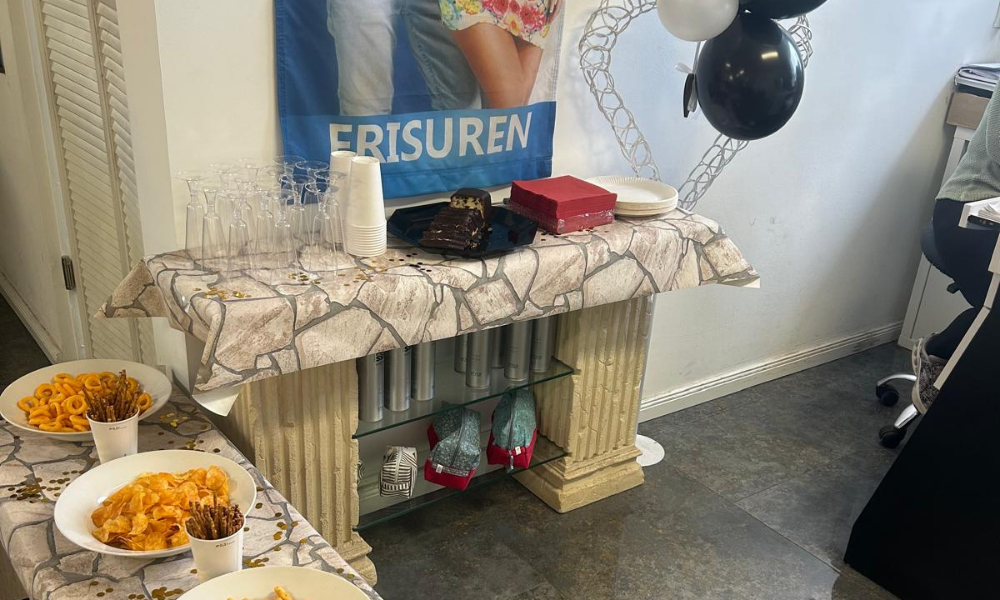 Buffet table with snacks and desserts, cups, and glasses, set under a banner and balloons at a party event