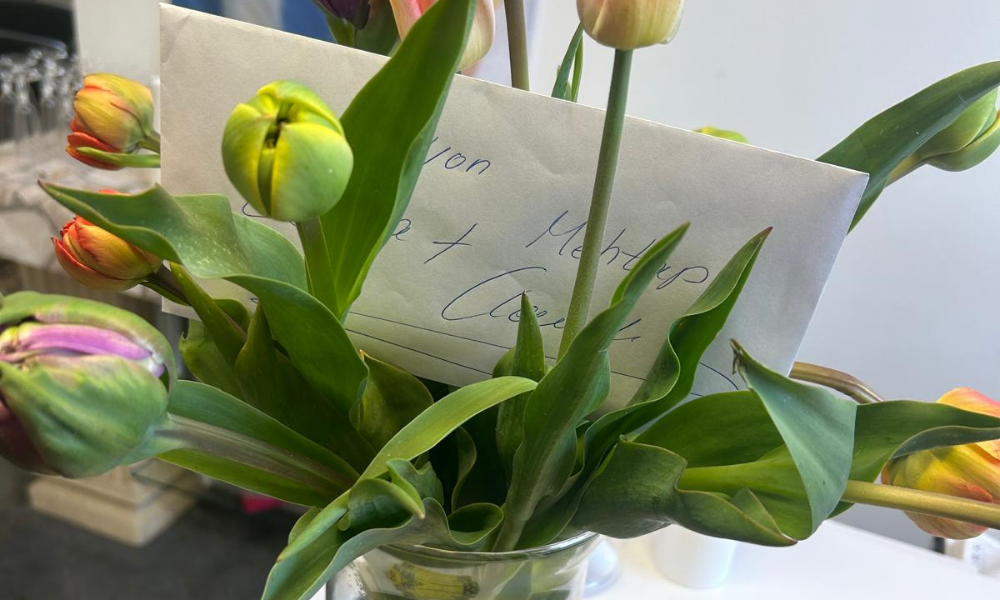 Bouquet of colorful tulips in a glass vase with a handwritten card tucked among the flowers.